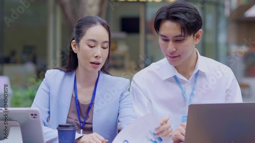 Colleagues, a team of business professionals, are working together or meeting, discussing work on laptops in front of the office.
