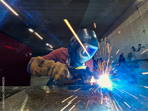 Professional Welder Using MIG-MAG Welding Process with Intense Orange Sparks and Blue Light in Workshop