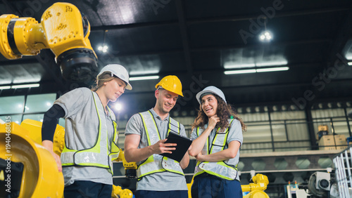 Diverse engineers collaborating, discussing modern factory automation with robotic arm technology. Industrial manufacturing team working on innovation, production, smart engineering solutions