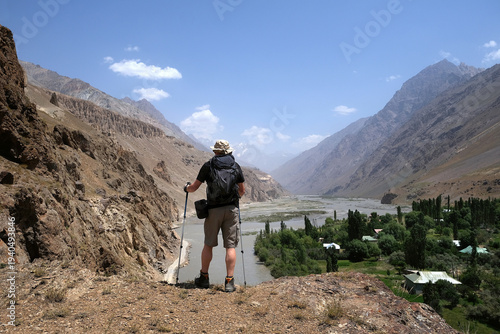 Bartang, Tajikistan - Panorama of Pamir Mountains with silhouette of standing man with backpack on trail around Siponj with green valley Bartang by river Bartang in background, Gorno Badakhshan