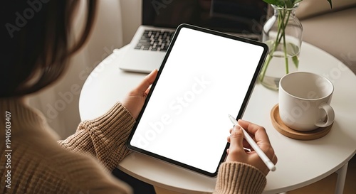 Person holding tablet with stylus on blank screen, cozy home workspace mockup design concept