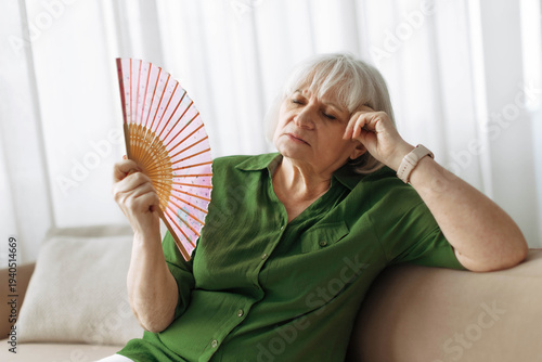 фотографія Senior woman cooling herself with handheld fan at home living room