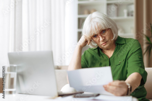 Senior woman looking worried while reading document at home. Mature caucasian female checking financial papers and managing personal matters during retirement lifestyle