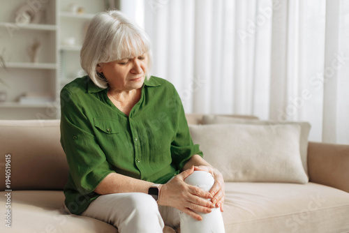 Canvastavla Senior woman holding painful knee while sitting on sofa at home