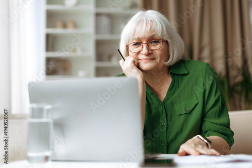 Senior woman looking at laptop screen with thoughtful expression at home. Mature caucasian female using technology for communication and online activity in relaxed retirement lifestyle
