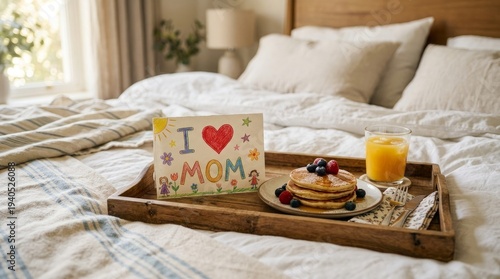 Delicious stack of fluffy pancakes with fresh berries and orange juice served on a tray with a handmade card for mom on a cozy bed