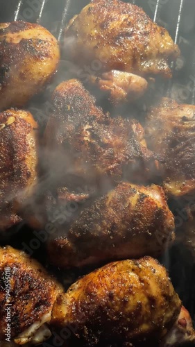 Vertical shot of many pieces of chicken thighs cooking on a grill with smoke rising off the pieces. The skin has an even char after being cooked on a barbecue grill.