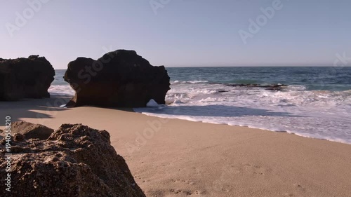 Gentle ocean waves wash over sandy beach with large rock formations