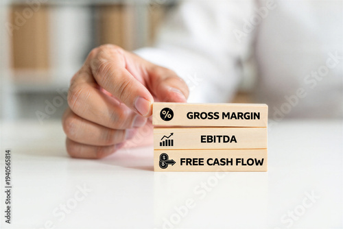 Hand stacking wooden blocks representing gross margin ebitda and free cash flow in a business context