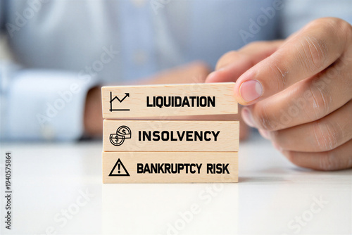 Hand stacks wooden blocks with financial terms liquidation insolvency and bankruptcy risk signifying business challenges and financial peril