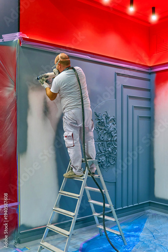 Construction worker spray painting interior wall using airless paint sprayer