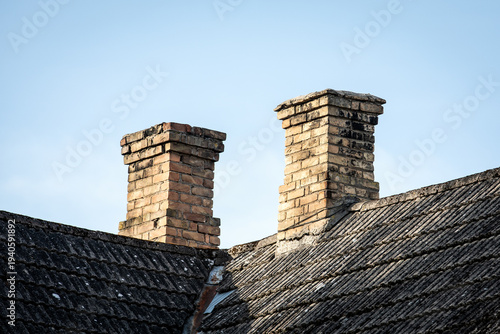 Two Brick Chimneys on Old Corrugated Roof Against Clear Blue Sky