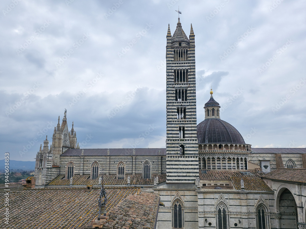 Fototapeta premium Siena Cathedral with the iconic striped bell tower and dome under a cloudy sky, medieval architecture, Tuscany, Italy