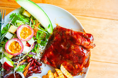 Close up of Baby spare ribs bbq, french fries, fruit, salad from top view on wooden table.A rack of delicious baby ribs barbecue sauce, passion fruit, melon salad at the restaurant. Special menu