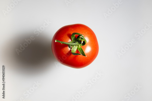 Studio photograph of a ripe red tomato seen from above with natural shadow on gray background. Concept of healthy nutrition, organic vegetables and minimal food composition. Authentic photography, not