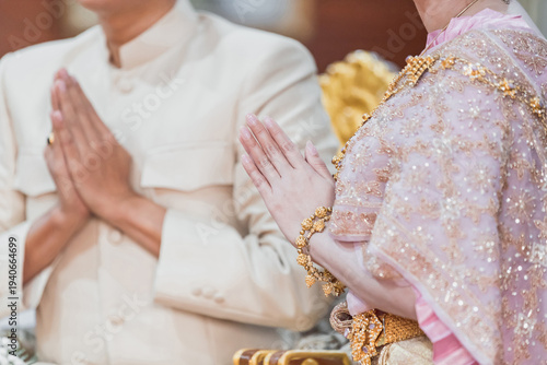 фотографія The bride and groom sit putting their hands together in a prayer position and dress in Traditional Thai Costumes
