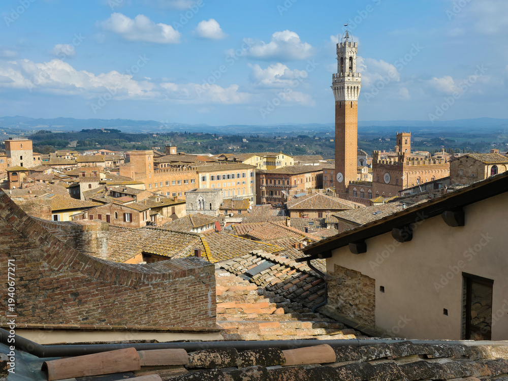 Fototapeta premium Panoramic Skyline of Siena with Torre del Mangia and Palazzo Pubblico, Italy. High Angle View of Medieval Rooftops in Tuscany under a Cloudy Blue Sky. Historic Italian Cityscape