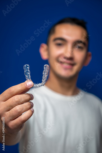 Young man smiling and holding a clear dental aligner, representing modern orthodontics and teeth straightening solutions