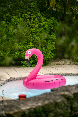 Foto Large pink flamingo pool float in a villa or resort swimming pool with green shrubs in the background