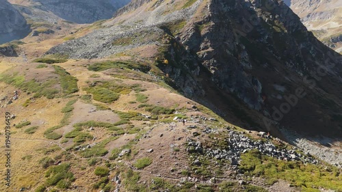 Rugged mountains stretch under golden sunlight. Slopes show wild grasses, rocks, and patches of green. No people are visible in this remote landscape