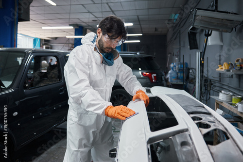 Schilderij op canvas Automotive technician sanding car body panel with orange gloves and protective c