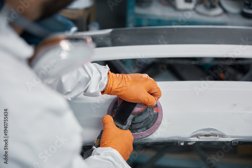 Foto The technician is sanding the car hood in the workshop, wearing safety gear for