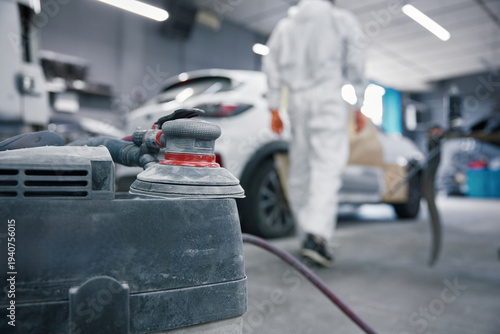 Auto body shop car painting prep with orbital sander and technician in protective suit