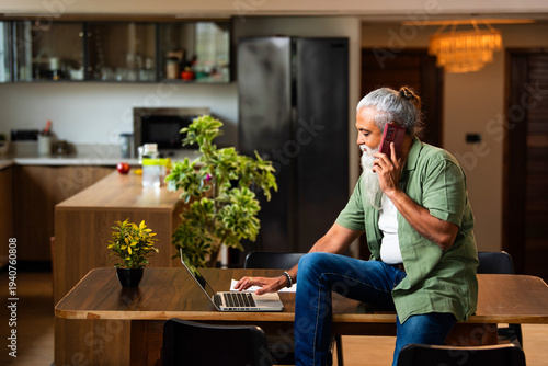 Modern Indian bearded man handling business call while working on laptop