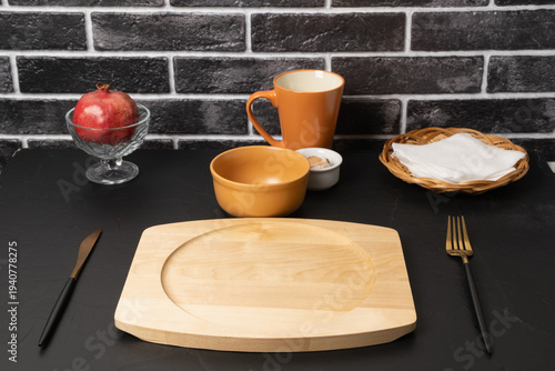 Table setting with bowls, cutlery, and fruit on a black surface in a kitchen environment