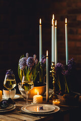 Beautiful elegant table setting for Easter celebration with fresh spring hyacinth flowers, burning candles. Romantic wedding dinner table decoration. Springtime, home gardening. Dark background