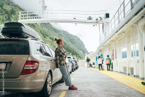 Wallpaper Mural Woman leans against her car on Norwegian ferry surrounded by other vehicles with misty green mountains in background. Scene captures essence of relaxed travel, exploration in scenic Norwegian fjords Torontodigital.ca