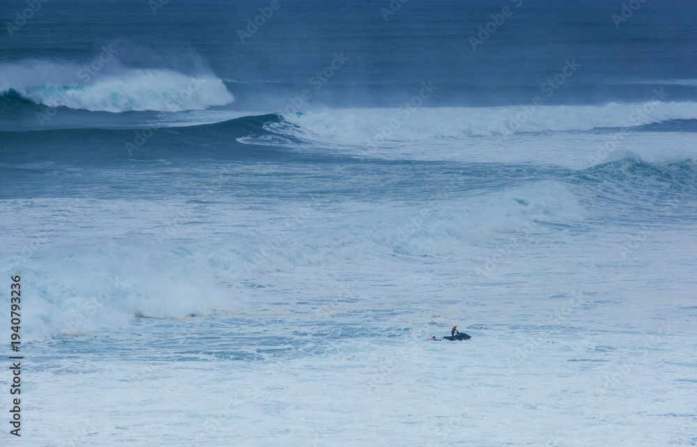 Fototapeta premium Sea doo rider providing safety support for big wave surfers during Nazare huge waves challenge with giant breaking Atlantic ocean swells in Portugal as symbol of extreme water sports and courage