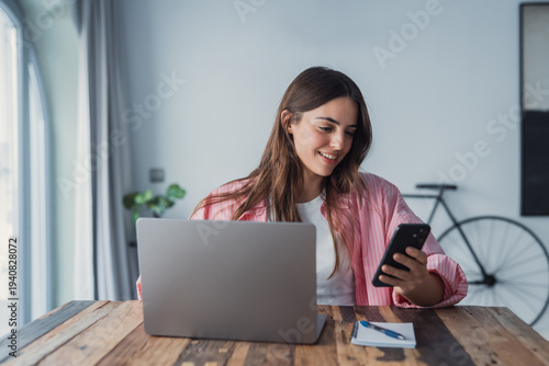 Photography A millennial businesswoman multitasks at home, using a laptop and smartphone to
