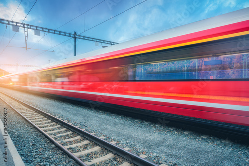 Konstfotografi Blurred red passenger train passing mountain railway station in Swiss Alps at sunset