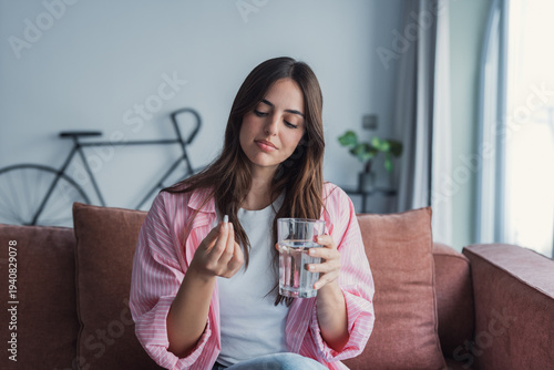 Foto A young woman smiles at home while taking a pill with a glass of water, practici