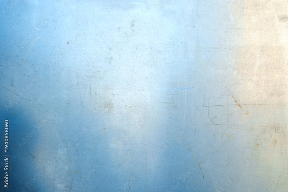 Obraz premium A horizontal close-up of a light blue metal sheet with visible scratches, small rust spots, and a bright light reflection on the surface.