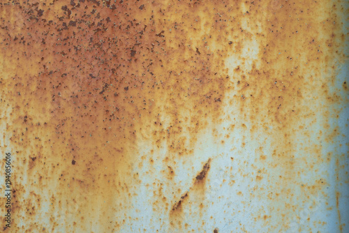 A horizontal close-up of a metal surface where heavy orange-brown rust has largely overtaken the original light blue paint.