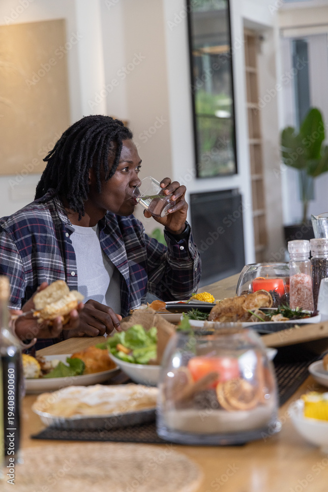 Fototapeta premium African American friends sitting at dining table at home drinking from glasses and sharing chicken