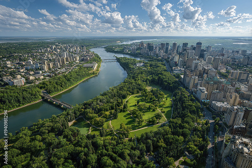 Aerial panoramic view of city skyline with river, bridges, and green parkland under blue sky with scattered clouds, showing urban and natural landscape harmony