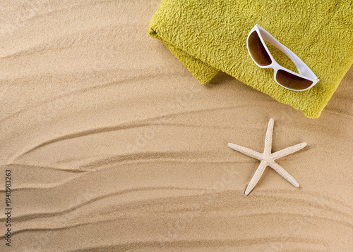 Beach towel and sunglasses on sandy beach, top view with space for text.