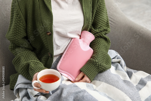 Photography Young woman with pink hot water bottle and cup of tea having menstrual cramps on