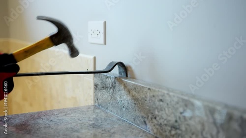 Worker removing old kitchen or bathroom furniture during home renovation using crowbar and hammer.