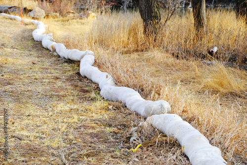 Erosion control tube along grassy roadside. Flood prevention equipment.