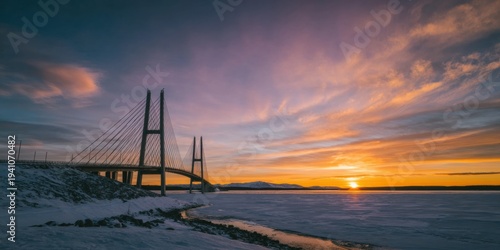 Suspension bridge silhouette at sunset over a frozen arctic landscape with snow and a colorful sky background for infrastructure and travel concepts with copy space