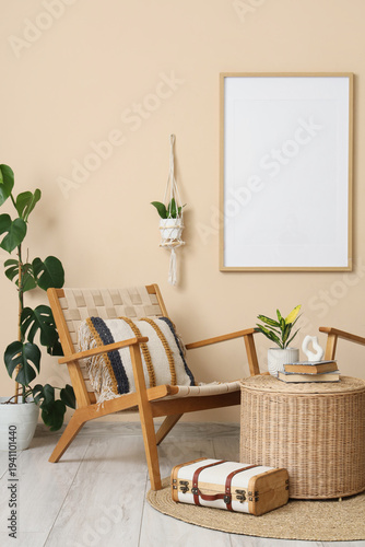 Interior of living room with armchair, houseplants, suitcase and books on wicker table near beige wall