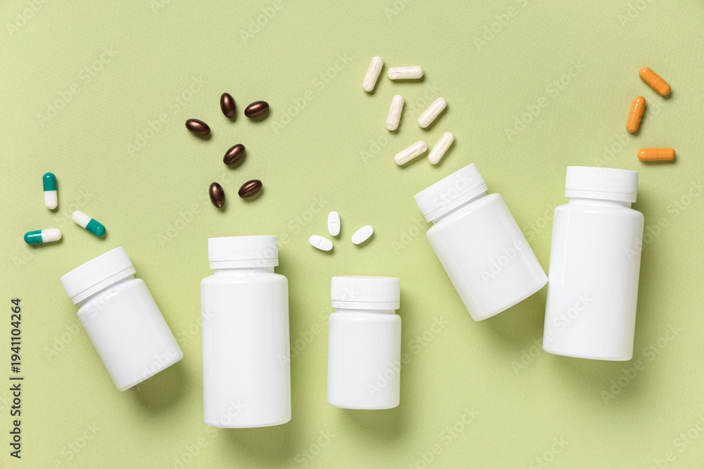 Fototapeta premium Blank plastic vitamin bottles and different pills on green background