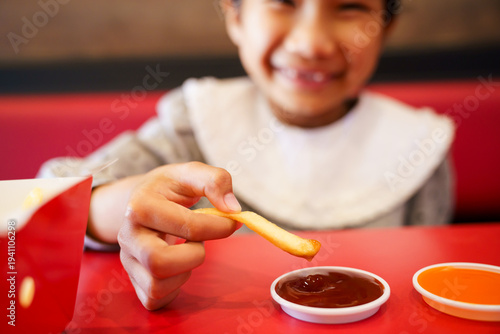 Asian girl dipping french fries into sauce at restaurant