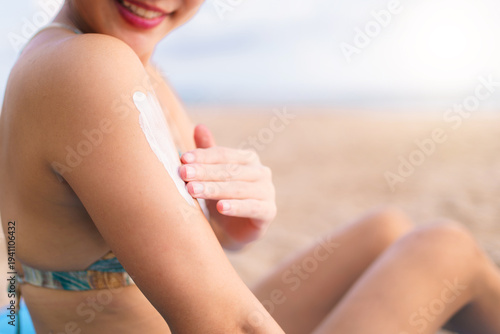Asian woman applying sunscreen on shoulder at the beach