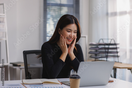 Young asian woman receiving exciting news on laptop