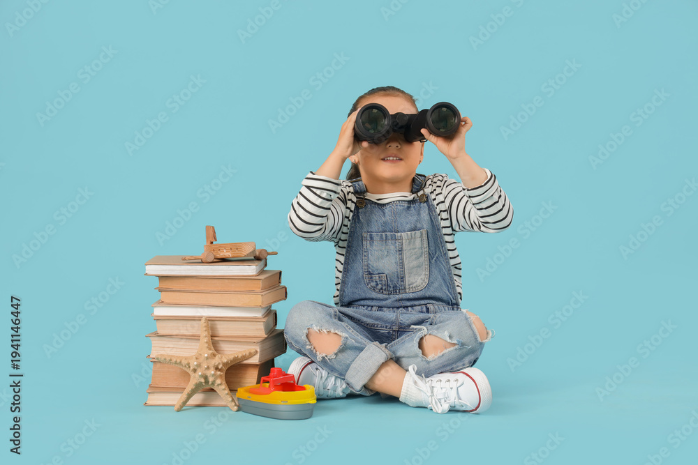 Naklejka premium Cute little girl with adventure books looking through binoculars on blue background